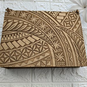 Puede incluir: Una caja de madera con un diseño polinesio tallado. El diseño es intrincado y presenta una variedad de formas geométricas y patrones.
