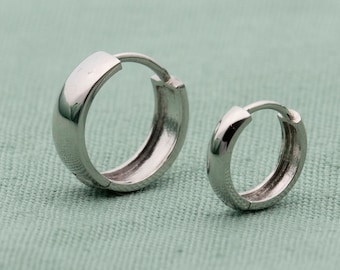 May include: Two silver hoop earrings, one larger than the other, on a green fabric background.