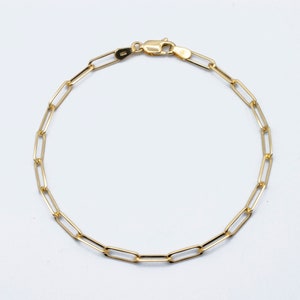 May include: A gold chain bracelet with a lobster clasp fastening. The chain is made of small, linked oval shapes.