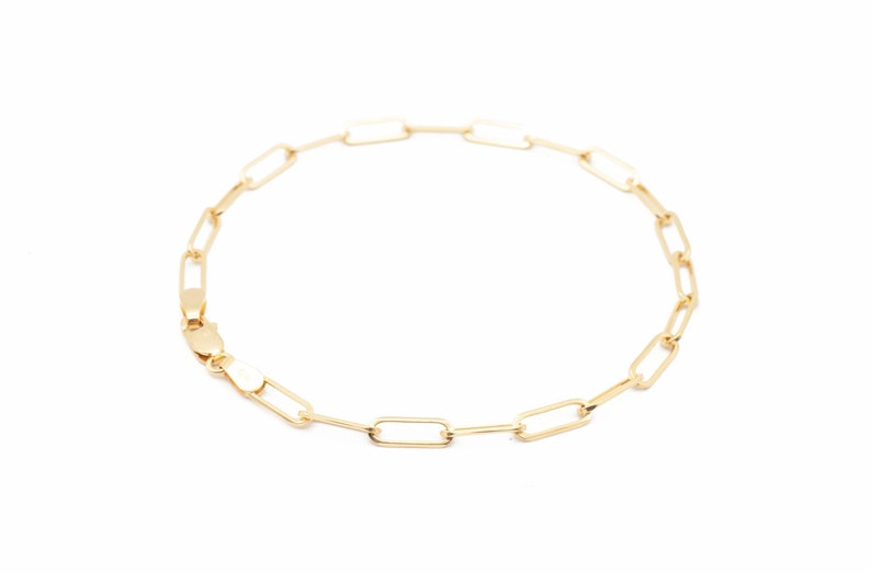 May include: A gold chain bracelet with a simple, linked design. The bracelet is made of small, rectangular links.