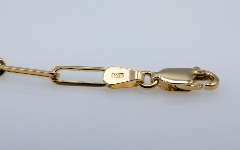 May include: Close-up of a gold chain with a lobster clasp. The chain is made of small, rectangular links. The clasp is stamped 14K.