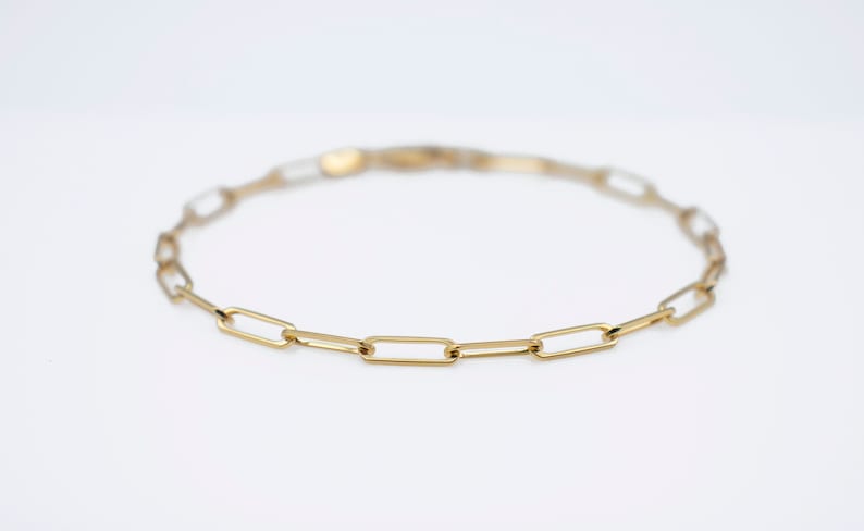 May include: A gold chain bracelet with a simple, linked design. The bracelet is made of small, rectangular links.