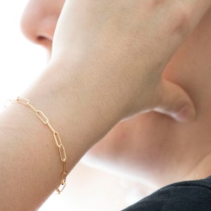 May include: A gold chain bracelet with a simple, linked design. The bracelet is worn on a person's wrist.