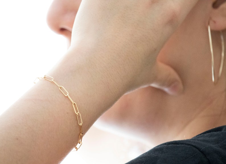 May include: A gold chain bracelet with a simple, linked design. The bracelet is worn on a person's wrist.