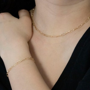 May include: A gold chain necklace and bracelet with a simple, linked design. The necklace is worn around the neck and the bracelet is worn on the wrist.