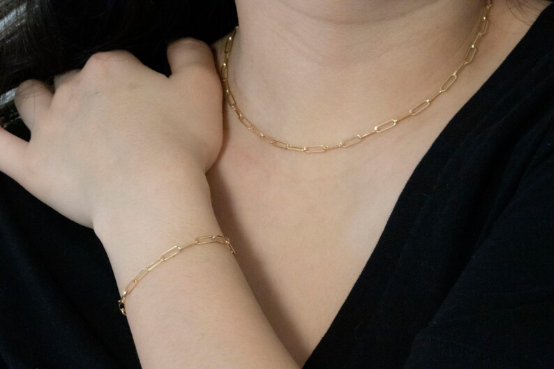 May include: A gold chain necklace and bracelet with a simple, linked design. The necklace is worn around the neck and the bracelet is worn on the wrist.