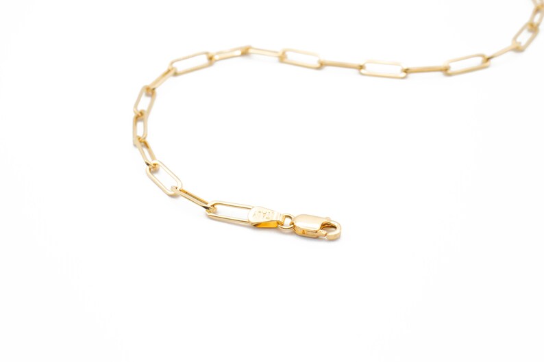May include: A gold chain necklace with a lobster clasp fastening. The chain is made of linked rectangular shapes.