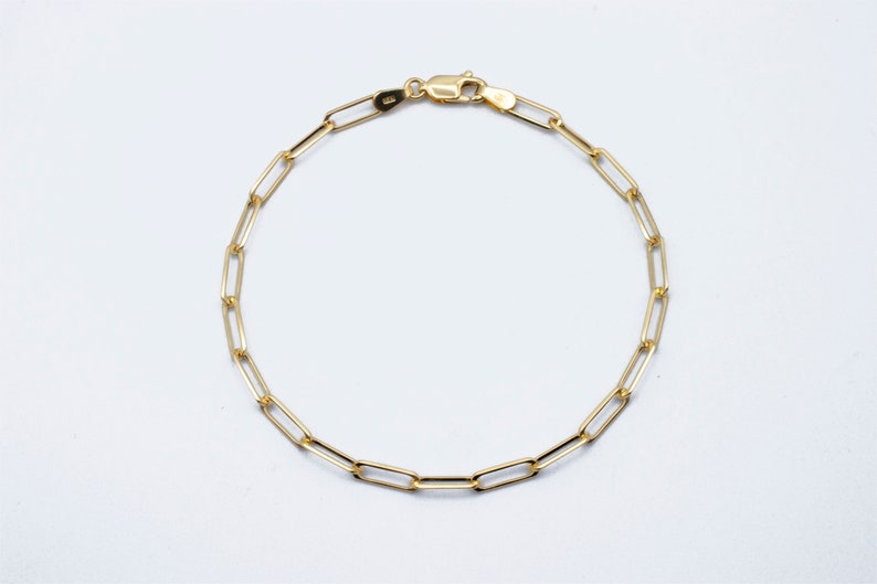 May include: A gold chain bracelet with a lobster clasp fastening. The chain is made of small, linked oval shapes.