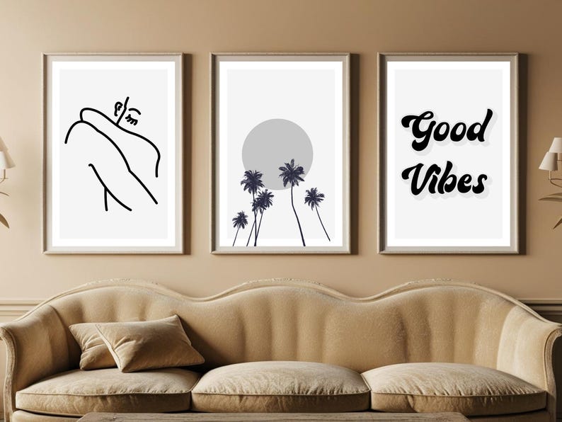 May include: Three framed art prints. The left print features a black line drawing of a person. The center print shows a gray sun and palm trees. The right print says "Good Vibes" in black script. The prints are above a beige sofa.