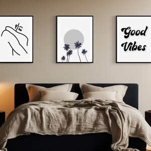 May include: Three framed wall art prints above a bed. The prints feature minimalist line art, a grayscale sun and palm trees, and the words "Good Vibes" in a script font. The bed has beige bedding and black nightstands with lamps.