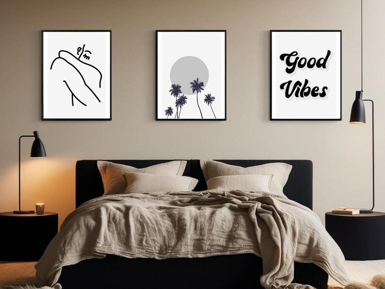 May include: Three framed wall art prints above a bed. The prints feature minimalist line art, a grayscale sun and palm trees, and the words "Good Vibes" in a script font. The bed has beige bedding and black nightstands with lamps.