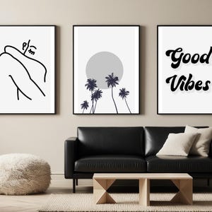 May include: Three framed art prints with black frames. The left print features a minimalist line drawing of a person. The center print shows palm trees in front of a gray sun. The right print says "Good Vibes" in black script.