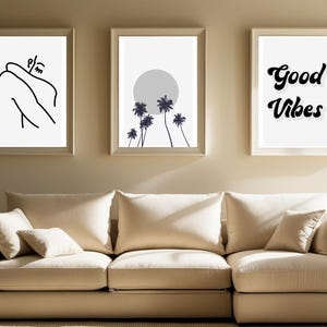 May include: Three framed art prints. The left print features a black and white line drawing of a person. The center print shows a gray sun and palm trees. The right print has the words "Good Vibes" in a black script font.