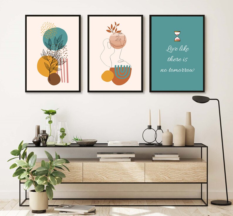 K&ouml;nnte beinhalten: Drei gerahmte Drucke mit abstrakten Designs in Braun-, Gelb-, Blaugr&uuml;n- und Rosat&ouml;nen. Der mittlere Druck zeigt eine Linienzeichnung eines Gesichts mit einem Blatt auf dem Kopf. Der rechte Druck hat einen blaugr&uuml;nen Hintergrund mit einer Sanduhr und dem Text "Lebe wie es kein Morgen gibt".