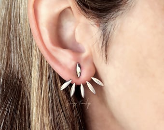 May include: Silver ear cuff earrings with a pointed design. The earrings are worn in the upper ear, with the points extending out from the earlobe.