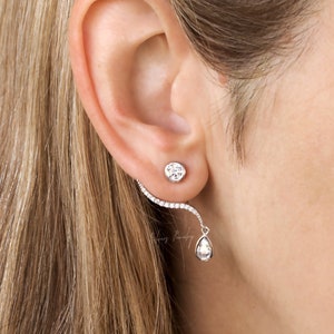 May include: A pair of silver earrings with clear cubic zirconia stones. The earrings are a drop style with a curved bar that goes up the ear.