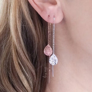 May include: A pair of delicate drop earrings with a textured teardrop design. The earrings are made of silver and rose gold and hang from a thin chain.