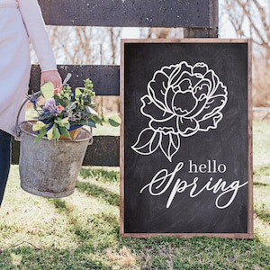 May include: A black chalkboard sign with a white outline of a peony flower and the text "hello spring" in white script.