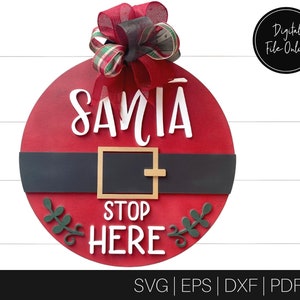 May include: Red and white Santa Claus door hanger with a black belt and the words "Santa Stop Here" in white lettering. The door hanger is decorated with a green and red bow.
