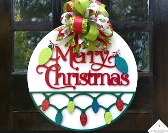 May include: White round wooden sign with the words "Merry Christmas" in red script. The sign is decorated with a green and red bow and a string of colorful lights.