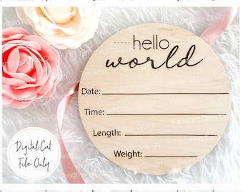May include: A laser-cut wooden circle with the text "hello world" and blank lines for "Date", "Time", "Length", and "Weight". The circle is surrounded by pink and white flowers and a pink ribbon.