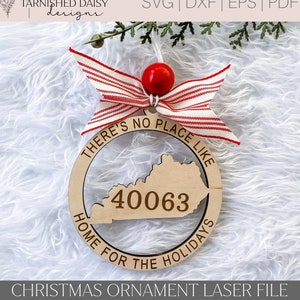 May include: A wooden Christmas ornament with a red and white striped bow. The ornament is shaped like a circle with a cutout of the state of Kentucky. The text "There's no place like home for the holidays" is written around the edge of the ornament. The number "40063" is written inside the cutout of Kentucky.