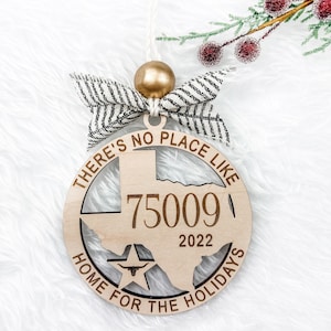 May include: A wooden Christmas ornament shaped like the state of Texas with the text "There's no place like home for the holidays" and the year "2022" and the number "75009" inside the state outline. The ornament is decorated with a black and white striped ribbon.