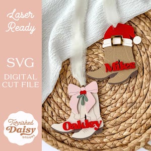 May include: Wooden laser-cut Christmas ornaments in the shape of cowboy boots. One boot has a Santa hat, the other has a pink bow. The names "Miles" and "Oakley" are in red. The text "Laser Ready", "SVG DIGITAL CUT FILE", and "Tarnished Daisy Designs" are also visible.