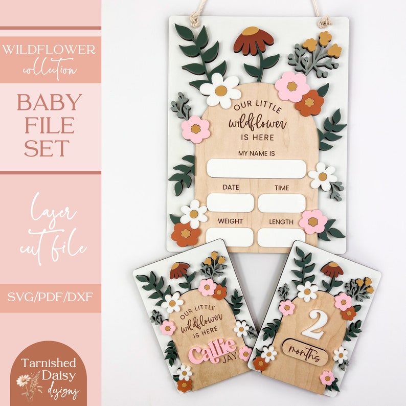 May include: A set of three wooden baby milestone signs with a floral theme. The signs feature a white background with green leaves, pink and white flowers, and a brown arch. The largest sign has spaces for the baby's name, date, time, weight, and length. The other two signs say "Our little wildflower is here Callie Jay" and "2 months".