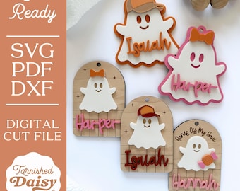 May include: A collection of laser-cut ghost-shaped name tags. The tags feature names like "Isaiah" and "Harper" in various colors, with some ghosts wearing hats or bows. The tags are made of wood and white acrylic, perfect for Halloween.