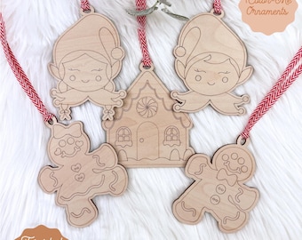 May include: Wooden Christmas ornaments in the shape of elves, a gingerbread house, and gingerbread people. Each ornament has a red and white striped ribbon for hanging. The text "Color-Me Ornaments" and "Digital Laser File" are visible.