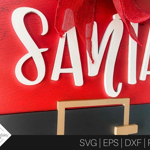 May include: A red and black Santa Claus door hanger with the word "SANTA" in white letters. The hanger has a gold-colored belt buckle.