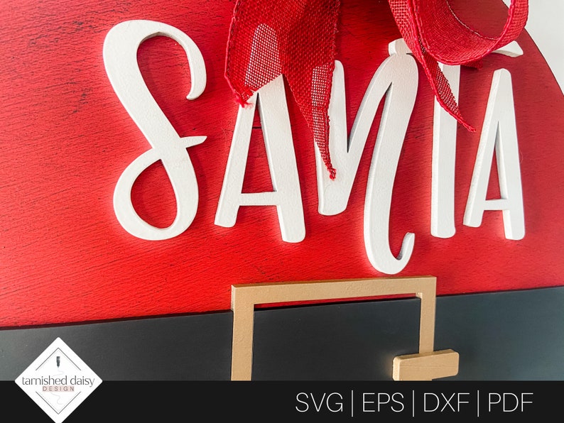 May include: A red and black Santa Claus door hanger with the word "SANTA" in white letters. The hanger has a gold-colored belt buckle.
