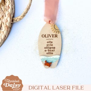 May include: Wooden surfboard-shaped ornament with the name "OLIVER" and nicknames. Features a sun, beach scene with a crab, and a pink ribbon. The ornament is a digital laser file.