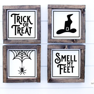 May include: Four wooden framed signs with black Halloween-themed text and images. The signs read "Trick or Treat", "Smell My Feet", a witch's hat, and a spider web with a spider.