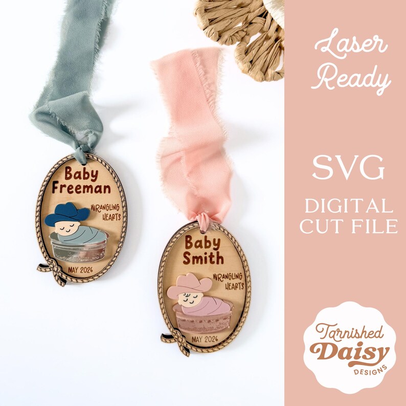 May include: Two wooden oval ornaments with baby-themed designs, each with a ribbon. One features a blue cowboy hat and the name "Baby Freeman," the other a pink cowboy hat and "Baby Smith." Both say "Wrangling Hearts" and "May 2026."