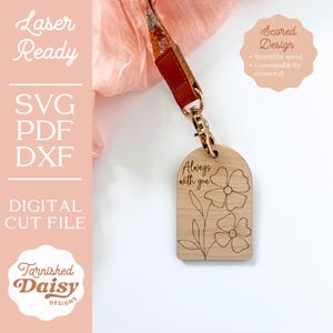 Puede incluir: Un llavero de madera con un acabado marr&oacute;n claro, que presenta el texto "Always with you" y un dise&ntilde;o floral. El llavero est&aacute; unido a un anillo de metal dorado.