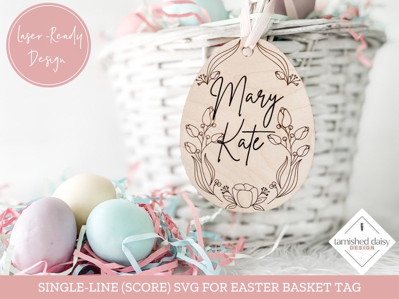 Puede incluir: Una etiqueta de cesta de Pascua de madera cortada con l&aacute;ser en forma de huevo con un dise&ntilde;o floral y los nombres "Mary Kate" escritos en una sola l&iacute;nea.