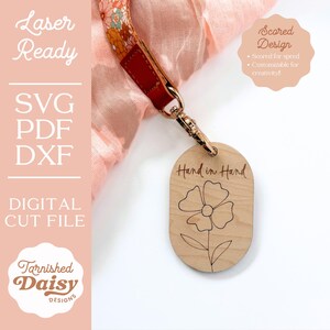 Puede incluir: Un llavero de madera con un dise&ntilde;o de flor y el texto "Mano a mano" grabado en &eacute;l. El llavero est&aacute; unido a un anillo de metal dorado.