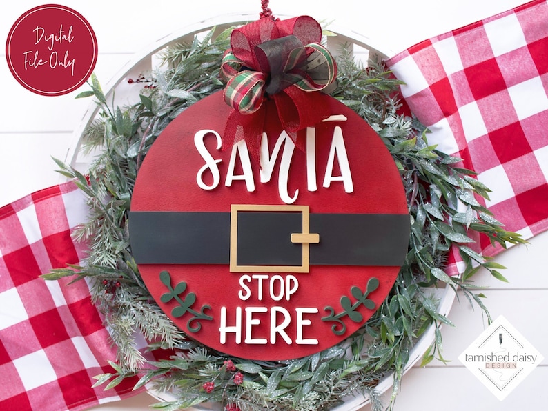 May include: A red and white Christmas wreath with a Santa Claus-themed sign that says "Santa Stop Here". The sign is made of wood and has a black belt with a gold buckle. The wreath is decorated with green leaves and red berries.