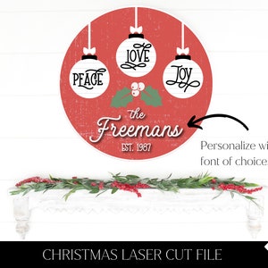 May include: Red circle with white ornaments that say "Peace", "Love", and "Joy" with holly and berries. The text "the Freemans Est. 1987" is below the ornaments.  This is a Christmas laser cut file.