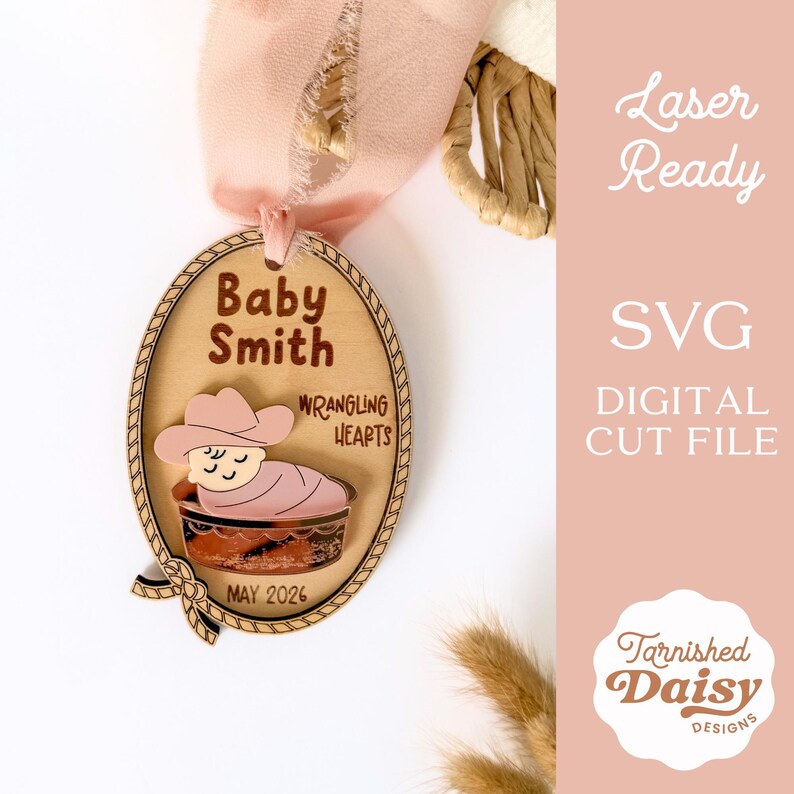 May include: Wooden baby announcement ornament with a cowboy theme. The oval-shaped ornament features the name "Baby Smith" and the phrase "Wrangling Hearts." A baby wearing a cowboy hat is in a bassinet. The date "MAY 2026" is printed on the bottom.