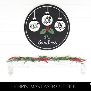 May include: Black circular sign with three white ornaments that say "Peace", "Love", and "Joy".  The sign also has a green holly sprig with red berries and the text "The Sanders".