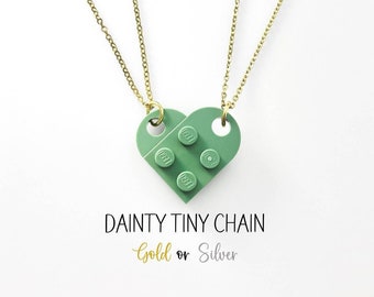 May include: Two delicate gold chains with a green heart-shaped pendant made of Lego bricks. The pendant has the text "LEGO" on it. The text "DAINTY TINY CHAIN Gold or Silver" is below the pendant.