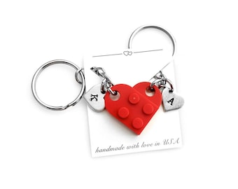 May include: A red Lego heart-shaped keychain with two silver heart charms attached. The charms are engraved with the letters "K" and "A". The keychain is attached to two silver key rings. The card reads "handmade with love in USA".