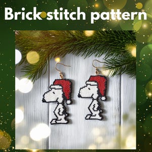 May include: Handmade Snoopy earrings in a brick stitch pattern, each wearing a red Santa hat. The earrings have gold-coloured hooks and are set against a white wooden background with a green and gold bokeh effect. The text "Brick stitch pattern" is at the top.