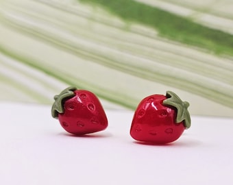 May include: A pair of red strawberry stud earrings with green leaves. The earrings are small and delicate, perfect for adding a touch of whimsy to any outfit.