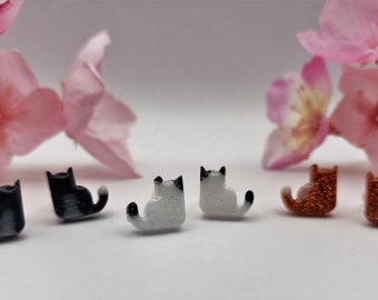 Puede incluir: Un conjunto de seis pendientes con forma de gato. Dos son negros con detalles blancos, dos son blancos con detalles negros y dos son de cobre con purpurina.