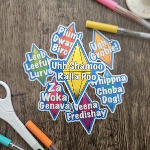 May include: A collection of colorful stickers with text, including phrases like "Ugh Groble!" and "Choba Dog!" The stickers are in various shapes, with a central yellow diamond design. Pens and scissors are visible in the background.
