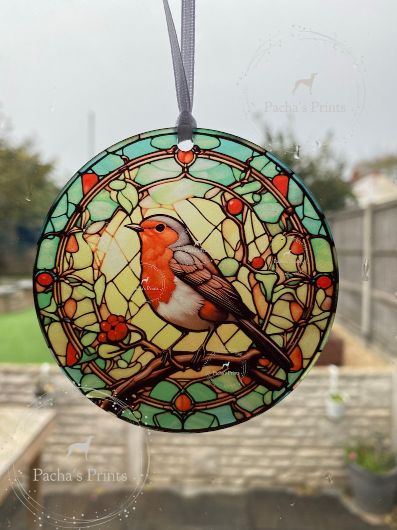 May include: A stained glass style round ornament featuring a robin perched on a branch with red berries. The ornament has a green, blue, and yellow color scheme.